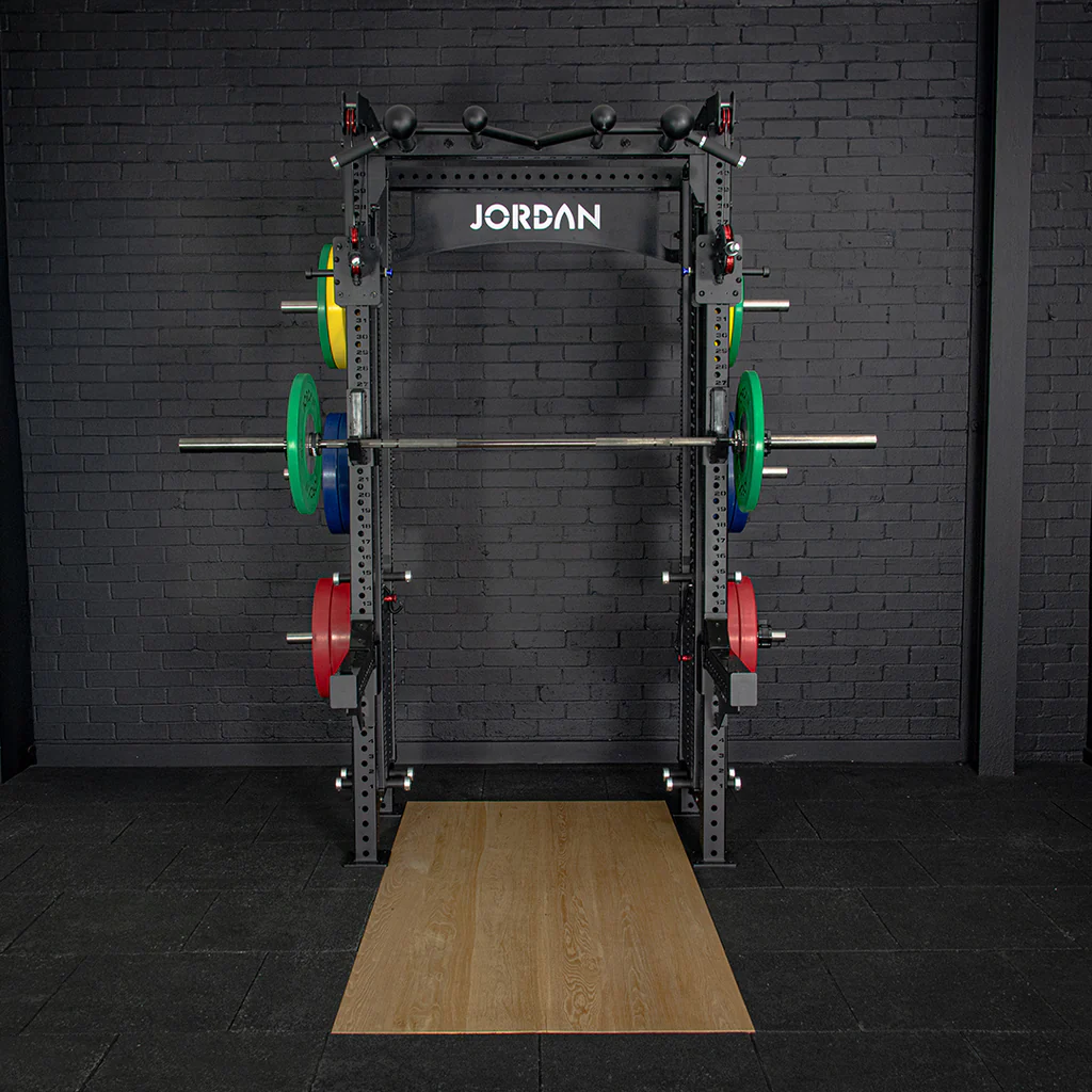 JORDAN® J75 Cable Rack Gym setting black brick background,  Barbell with Weights, Storage pegs with weights displayed, Spotter arms, Jordan olympic flooring front view