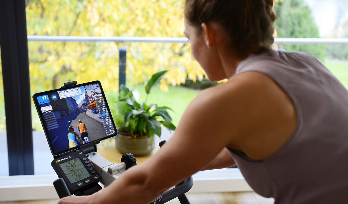 Concept 2 Bike Erg, lady using bike with her ipad displaying the tracking features. 